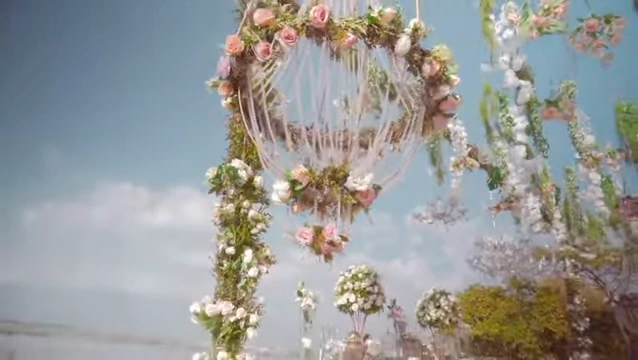 A hanging floral chandelier in white and blush with the lake and blue sky behind it, from The White Dream film